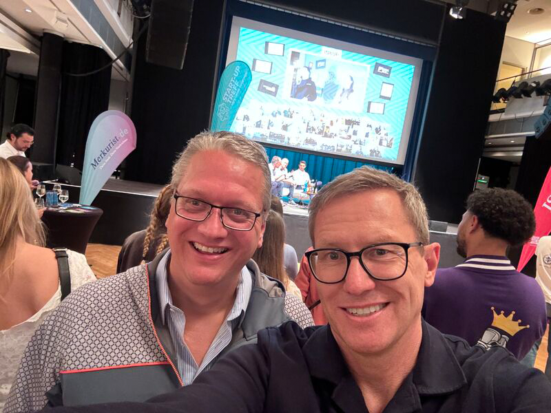 Selfie mit Michael Tonner und einer zweiten Person. Im Hintergrund eine Leinwand mit einer aktiven Folie.
